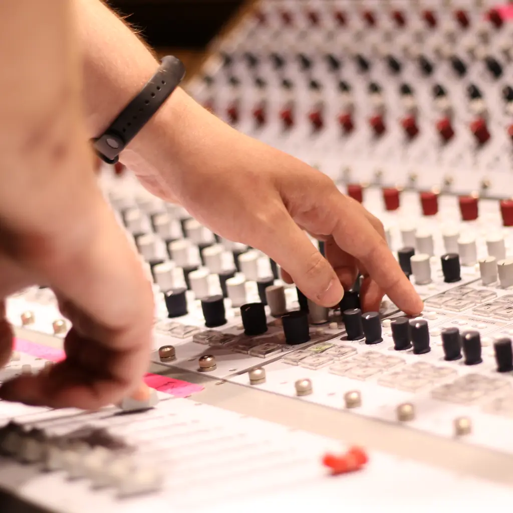 Hands adjusting faders on a mixing console.