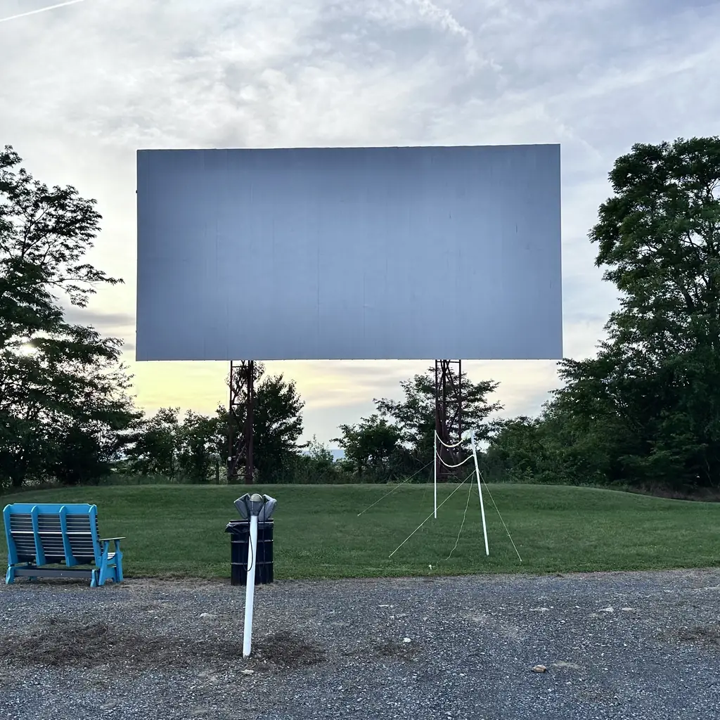 A drive-in theatre screen at dusk with cars parked in front.